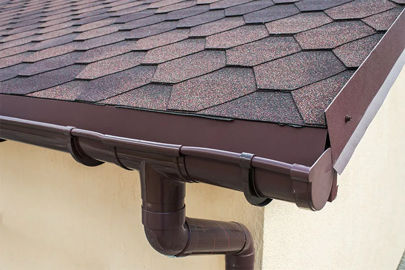 Brown half-round gutter and round downspout below hexagonal shingles