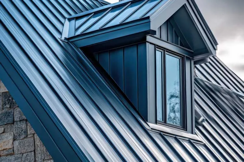 Dark blue standing seam metal roof with a dormer and a stone chimney