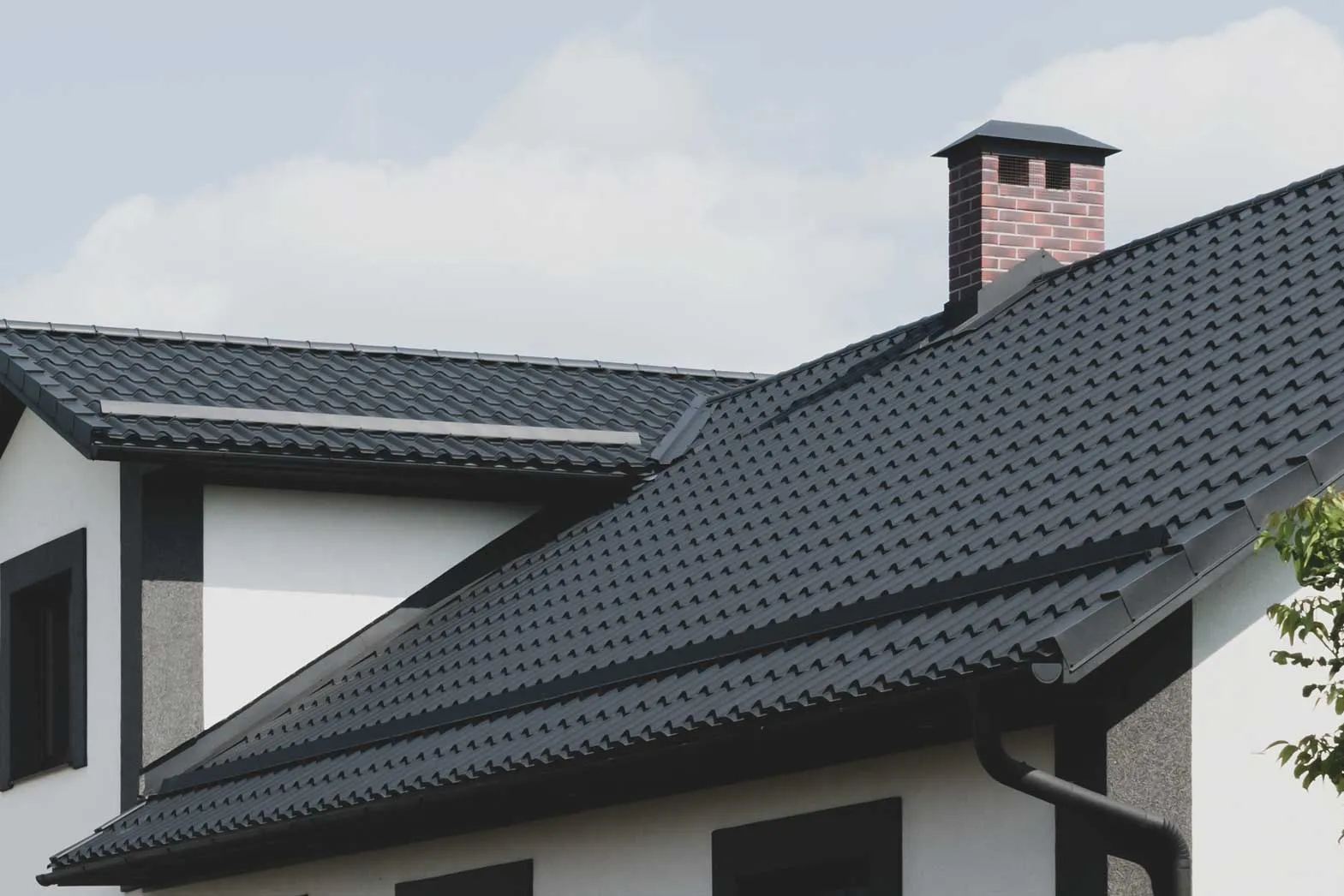 Dark stamped metal roof with a brick chimney on a white house