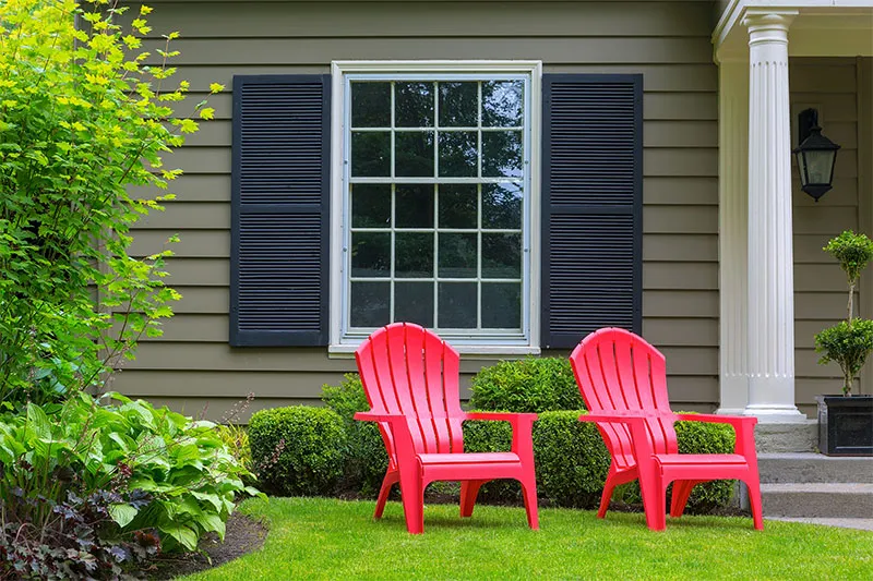 Double-hung window with black shutters on gray-green siding