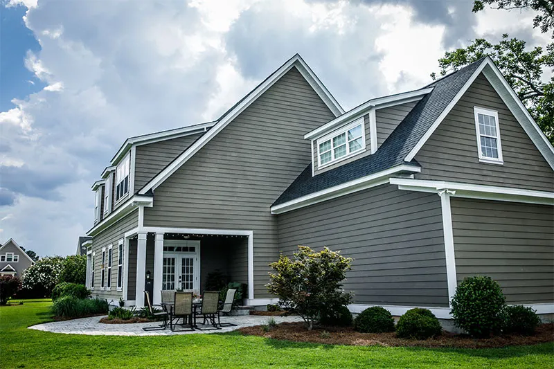 Two-story house with gray-green lap siding, dormers and a patio