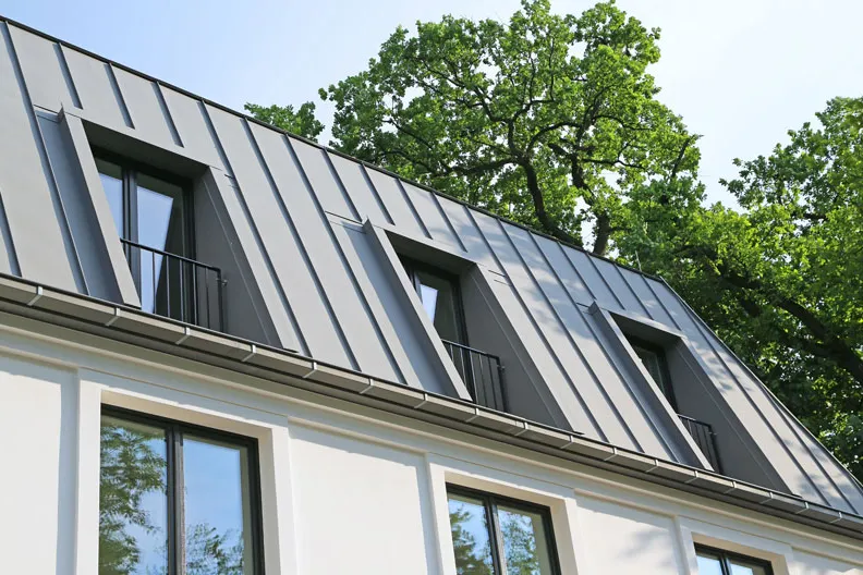Gray standing seam metal roof with dormers on a mansard-style house