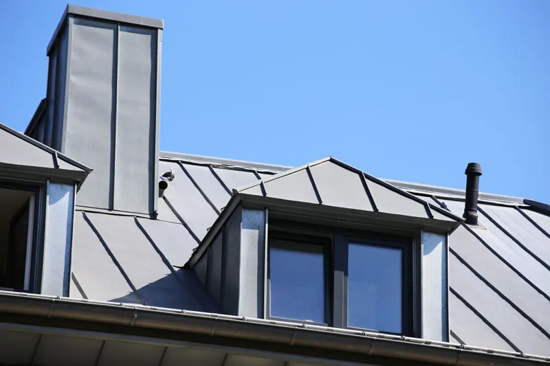 Gray standing seam metal roof with a dormer and a tall chimney