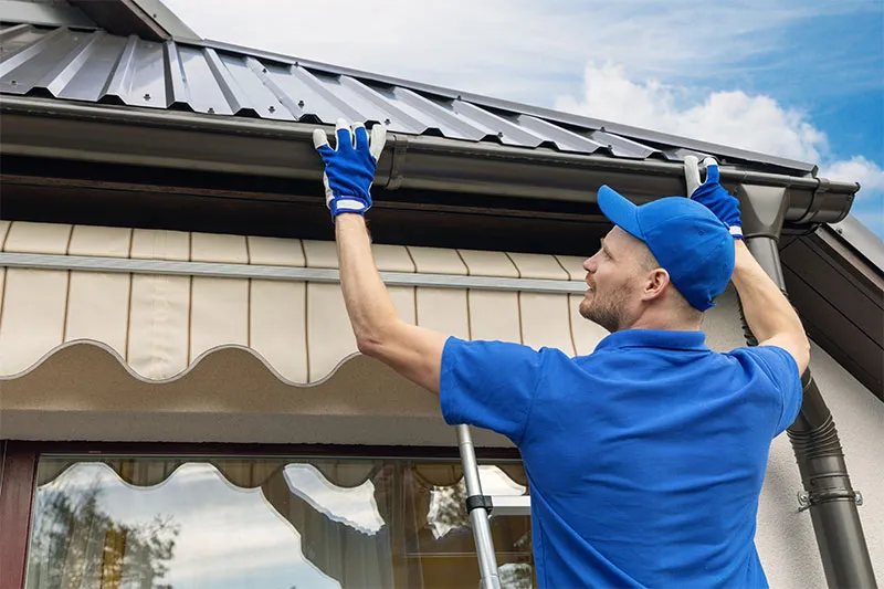 Installer in a blue cap and gloves fitting a gutter along a roof edge