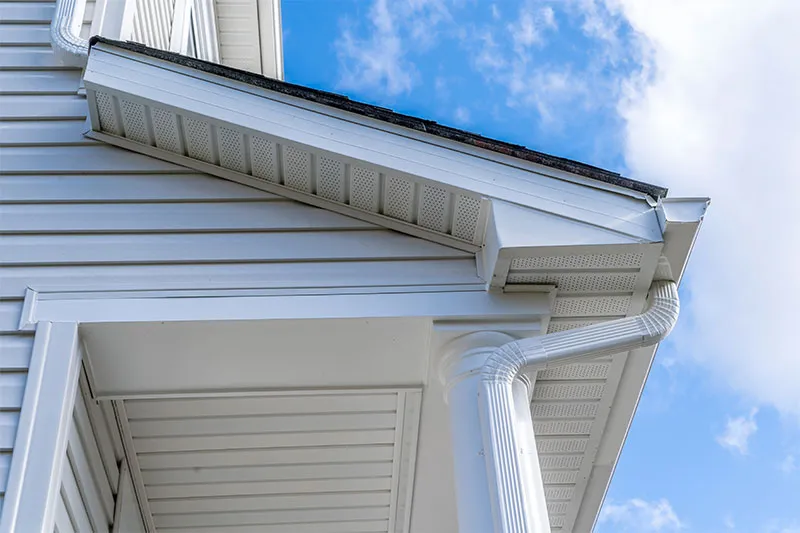 White gutter, downspout, fascia and vented soffit at the corner of a house with light siding
